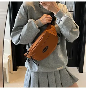 Detailansicht einer braunen Brusttasche im Techwear-Stil mit Logo-Patch, getragen von einem Modell