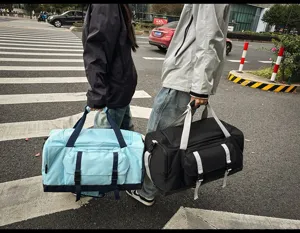 Due persone che trasportano borse da viaggio bicolore di grande capacità in città