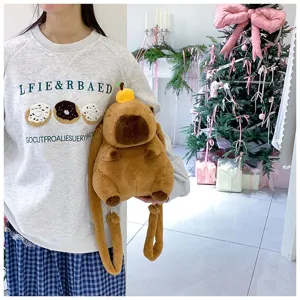 Cute plush capybara backpack with orange detail held by a model in cozy setting