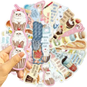 Close-up of a hand holding a cute cat cupcake bookmark with a blurred set background.