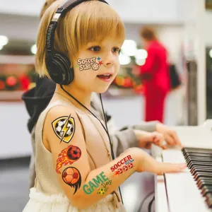 Child showing soccer temporary tattoos while playing piano in a warm indoor setting