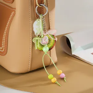 Gedetailleerd aanzicht van een acryl kiwi tasbedel met een groene strik en kralen