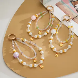 Close-up of iridescent beaded phone charms with gold crown and charm details.