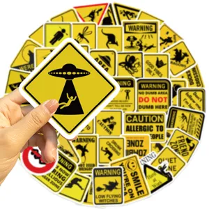 Close-up of funny yellow warning stickers featuring a UFO abduction design held by hand.