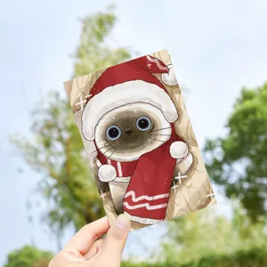 Detailed view of a cute cartoon cat Christmas postcard held against a nature backdrop