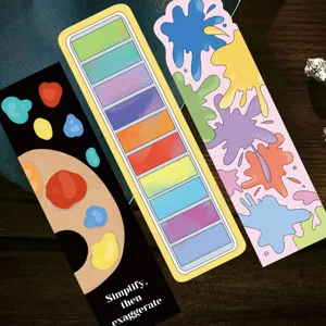 Detail showing three colorful art-themed paper bookmarks on a dark wood background