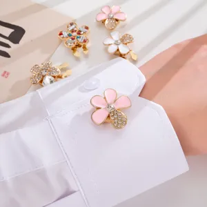 Close-up of a pink enamel flower pin with rhinestones on a white shirt sleeve cuff.