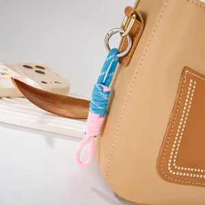 Detailaufnahme eines blau-rosa geflochtenen Nylon-Taschenanhängers an Ledertasche.