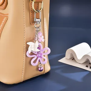 Nahaufnahme eines lila Blumenanhängers und weißen Windrads an einer braunen Tasche