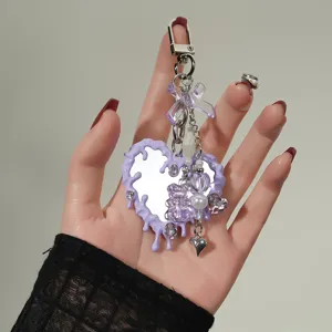 Primer plano de llavero con espejo en forma de corazón morado y colgantes de oso y lazo.