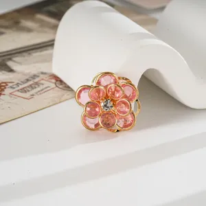 Dettaglio macro di un ciondolo a forma di camelia rosa con bordo dorato e strass centrale