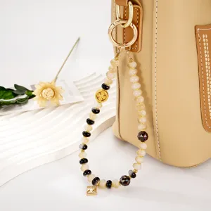 Close-up of handmade beaded wrist strap with golden square pendant and flower charm