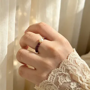 Nahaufnahme eines elastischen Rings mit Granatperlen und Naturperle an der Hand.