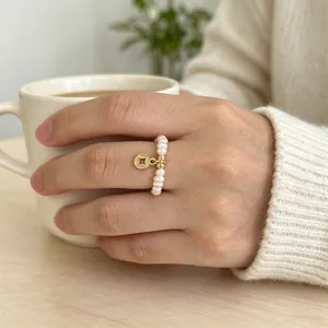 Nahaufnahme eines natürlichen Süßwasserperlenrings mit goldenem Münzanhänger an der Hand.