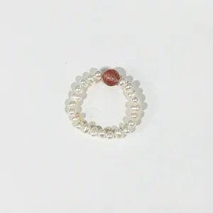 Close-up view of an elastic freshwater pearl ring featuring a red strawberry crystal bead