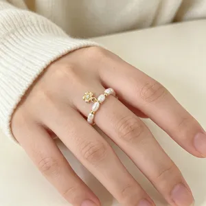Detailansicht eines elastischen Süßwasserperlenrings mit goldenem Blumenanhänger.