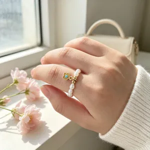 Detailansicht eines eleganten Süßwasserperlenrings mit goldenem Blumenanhänger am Finger