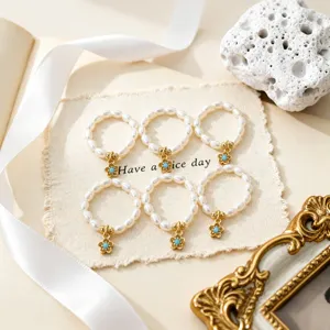 Detailansicht von sechs elastischen Süßwasserperlenringen mit goldenen Blumenanhängern.