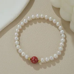 Detailaufnahme eines natürlichen Süßwasserperlenarmbands mit roter Cinnabar-Perle und Goldakzenten.