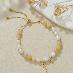 Nahaufnahme des verstellbaren Perlenarmbands mit goldenem Schlüssel und Herz-Anhänger.