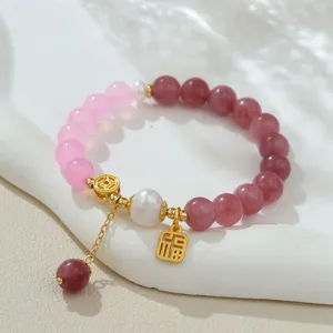 Gros plan détaillé d'un bracelet en perles naturelles, agate rose et breloques dorées de style chinois.