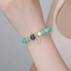 Gros plan détaillé du bracelet de perles vertes élégantes avec breloque dorée et perle blanche.