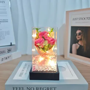 Detailed view of artificial rose flower bouquet in a clear acrylic box with warm LED lights.
