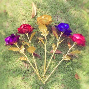 Close-up detail of artificial gold foil rose flower with golden stem on natural grass.
