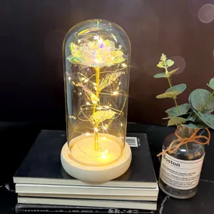 Close up of glowing gold foil rose in glass dome with fairy lights on wooden base and decor.