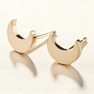 Gold crescent moon stud earrings detail close up, minimalist geometric jewelry style.