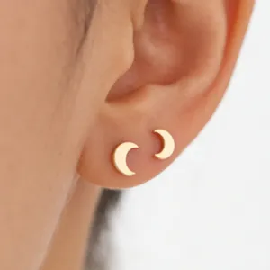 Close-up detail of minimalist gold crescent moon stud earrings worn delicately on earlobe.