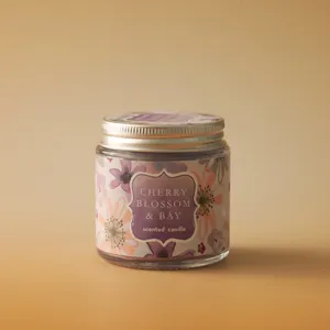 Detail close-up shot of glass jar scented candle featuring floral label and metal lid.