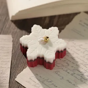 Snowflake scented soy wax candle detail view, featuring red and white layers and a gold bell.
