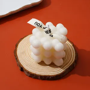 Detalle en primer plano de vela aromática blanca con cinta sobre posavasos de madera.