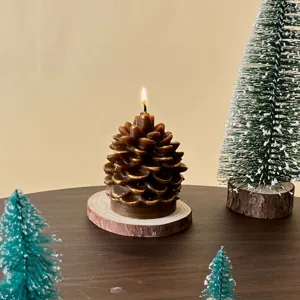 Close-up detail of a burning pinecone scented candle with gold trim on a wooden slice.