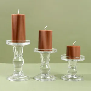 Vista detallada de velas de pilar acanaladas marrones con candeleros de vidrio transparente.