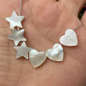 Gros plan détail du beau collier de charme étoile et cœur en nacre naturelle sur main.