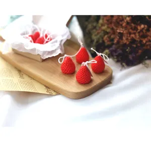 Detailed closeup view of cute mini strawberry scented candles set on a rustic wooden board.