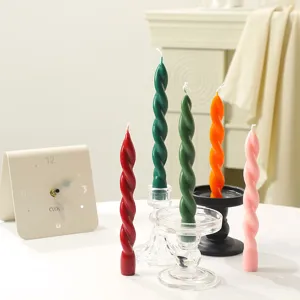 Nahaufnahme von bunten, gedrehten Stumpenkerzen auf Glas- und schwarzen Haltern für Deko.