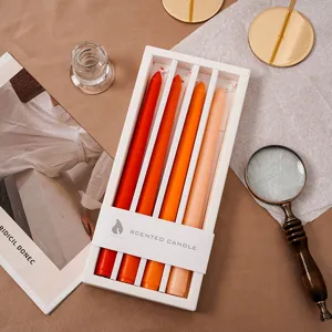 Detailansicht von duftenden Stabkerzen mit Farbverlauf in weißer Geschenkbox mit warmen Requisiten.