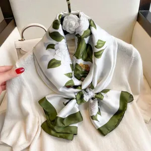 Closeup of white silk scarf with green leaves and camellia floral pattern, elegant drape.