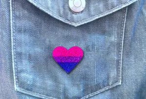 Gros plan d'une broche cœur à paillettes colorées épinglée sur une poche en jean, accessoire.