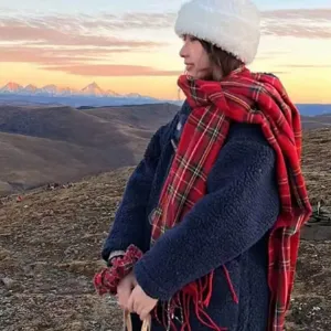 Outdoor detail shot of a stylish red plaid winter warm scarf and cozy fleece outerwear.