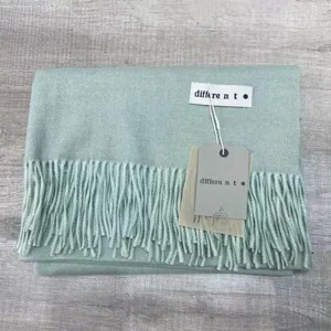 Gros plan détaillé de l'écharpe d'hiver douce vert clair avec texture et étiquettes de marque.