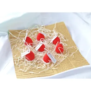Mini strawberry scented candles set with decorative tags on paper filler, perfect gift.