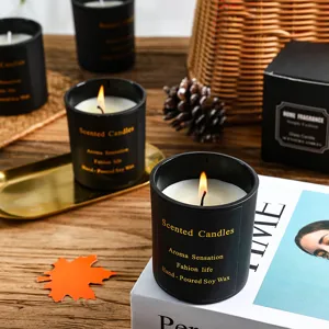 Detail view of black scented jar candles with warm glowing flame and elegant autumn decor.