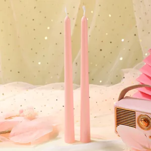 Gros plan de deux bougies roses fines avec une radio rétro décorative sous un éclairage chaleureux.
