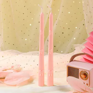 Gros plan détail de bougies parfumées roses coniques avec décor de nœud pour un dîner aux chandelles.
