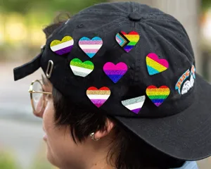 Vue rapprochée de badges et épingles cœur pailletés colorés LGBTQ+ sur une casquette noire.