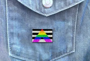 Gros plan détaillé d'un pin's émaillé drapeau arc-en-ciel ally sur une poche en jean.